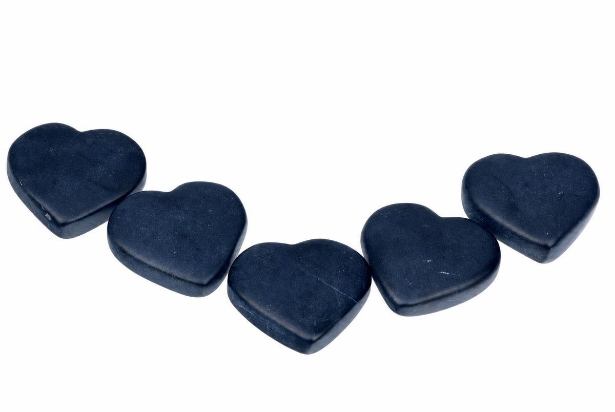 Five dark blue, heart-shaped massage stones arranged in a gentle curve on a white surface.