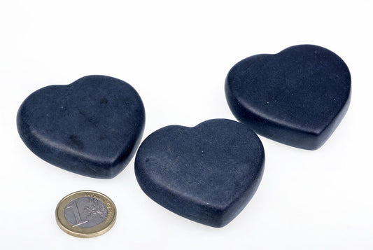 Three dark blue, heart-shaped massage stones on a white surface with a one-euro coin for scale.
