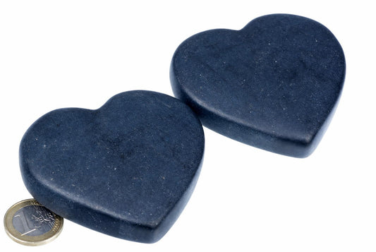 Two dark blue, heart-shaped massage stones on a white surface with a coin for scale.
