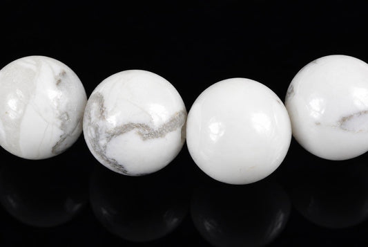 Four round beads of white and grey patterned stone on a dark surface.