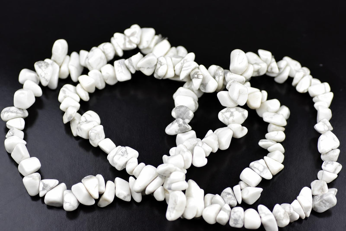 A white and grey speckled Howlite chip bracelet coiled on a dark surface.