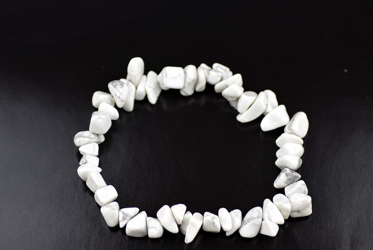 A bracelet made of white and grey howlite chips arranged in a circle on a dark surface.