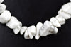 A necklace of white and grey speckled howlite chips arranged in a curved line on a dark surface.
