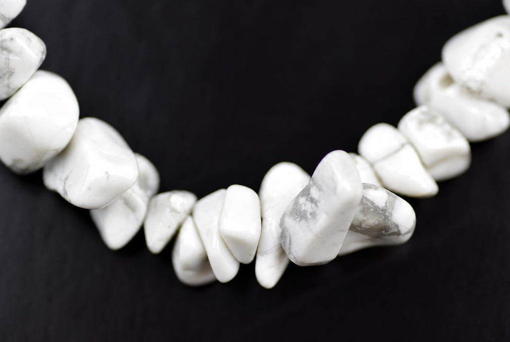 A necklace of white and grey speckled howlite chips arranged in a curved line on a dark surface.