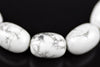 A close-up of white Howlite beads with grey veining, arranged on a dark surface.