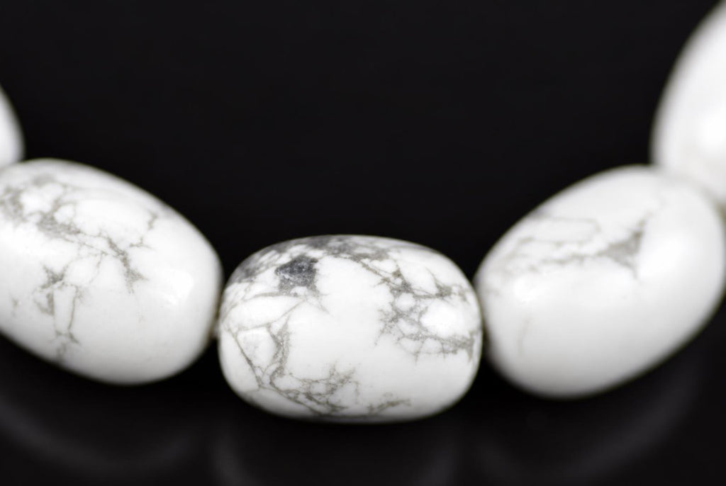 A close-up of white Howlite beads with grey veining, arranged on a dark surface.