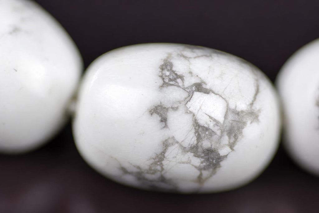 A close-up of a white, oval-shaped bead with grey veining, part of a bracelet on a dark surface.