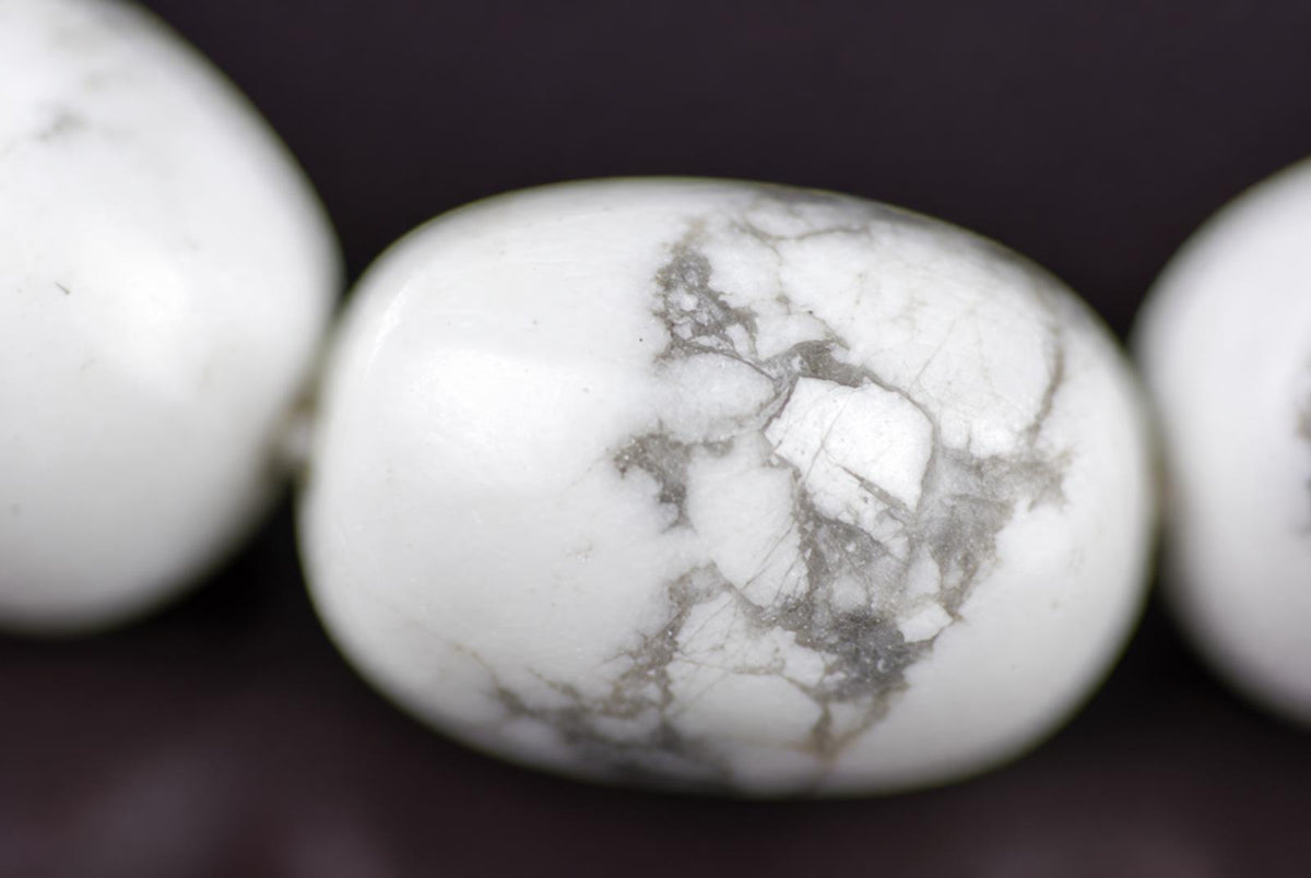 A close-up of a white, oval-shaped bead with grey veining, part of a bracelet on a dark surface.