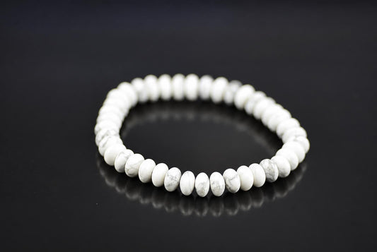 A white and grey patterned Howlite bracelet with round beads arranged in a circle on a dark surface.