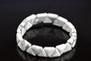 A bracelet made of white and grey veined triangular stones arranged in a circle on a dark surface.