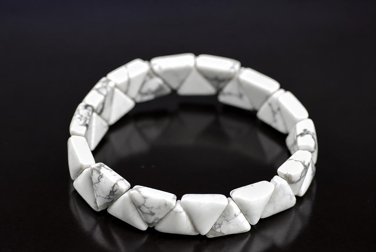 A bracelet made of white and grey veined triangular stones arranged in a circle on a dark surface.