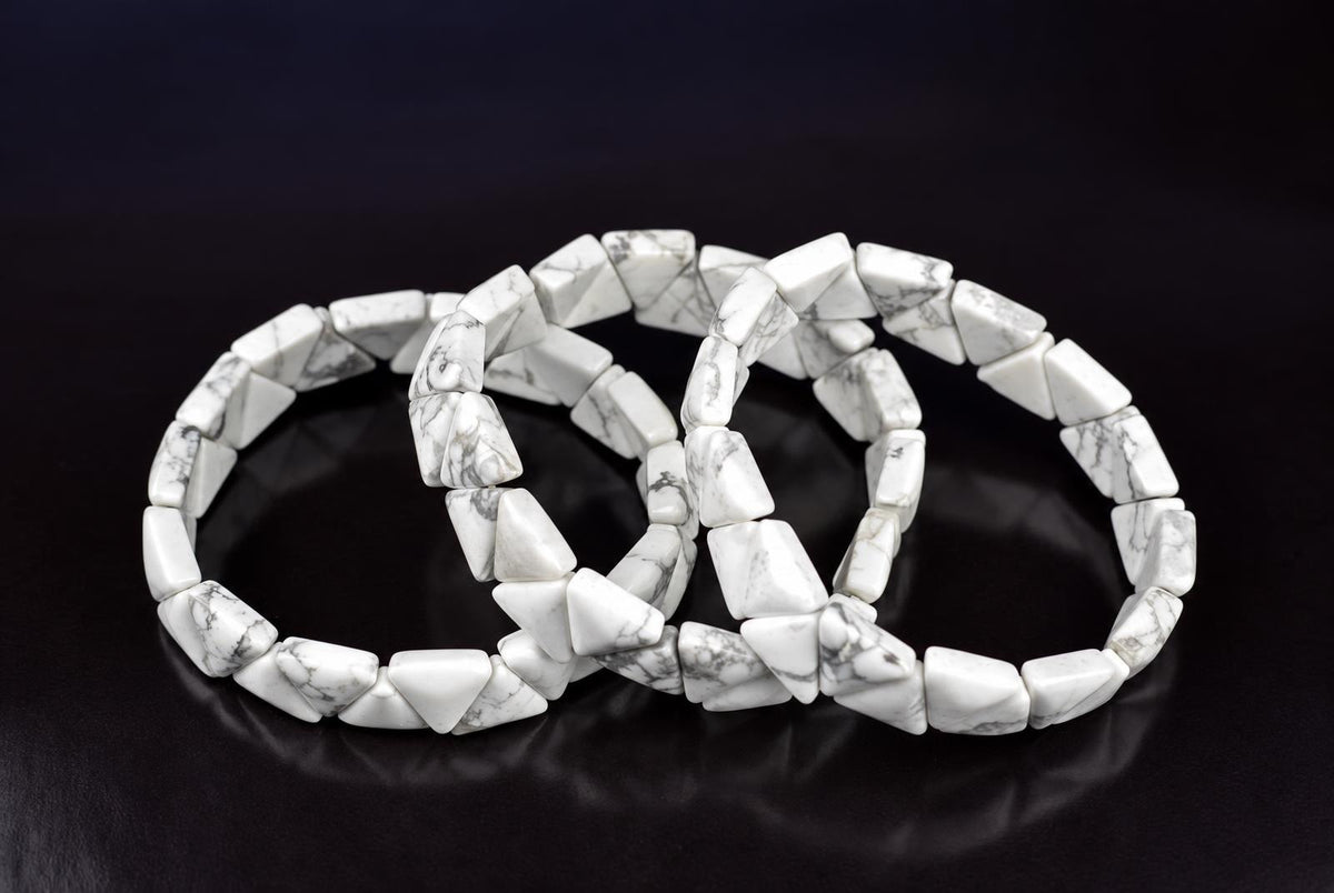 Two white and grey veined triangle-shaped bracelets lie on a dark surface.