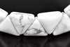 A close-up of a white and grey patterned Howlite bracelet with triangular beads on a dark surface.
