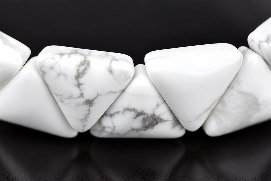 A close-up of a white and grey patterned Howlite bracelet with triangular beads on a dark surface.