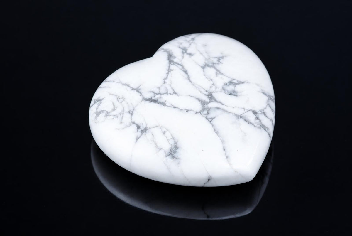 A polished, heart-shaped stone with white and grey veining rests on a dark surface.