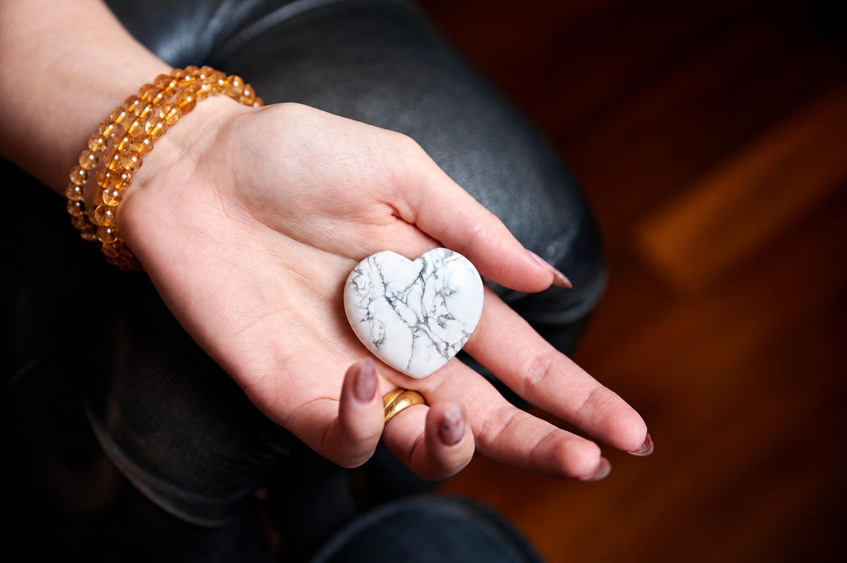 A hand holds a white heart-shaped stone with grey veins, resting on dark fabric.