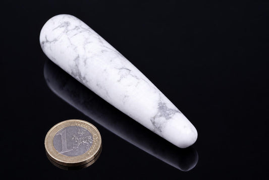 A smooth white massage stick with gray veining lies diagonally on a black surface beside a coin.