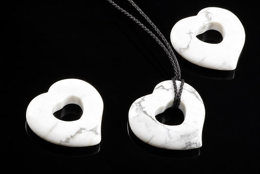 Three white heart-shaped pendants with grey veining, one on a dark cord, arranged on a black surface.
