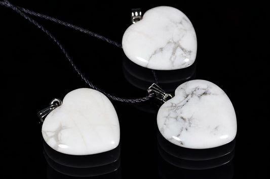 Three heart-shaped white pendants with grey veining hang on dark cords against a black reflective surface.