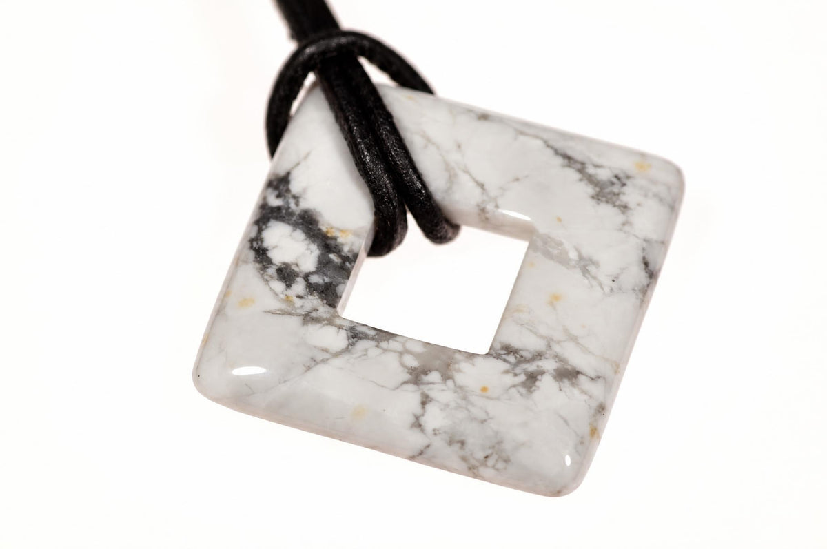 A square-shaped pendant with a central hole, featuring white and grey veined patterns, attached to a black cord against a white background.