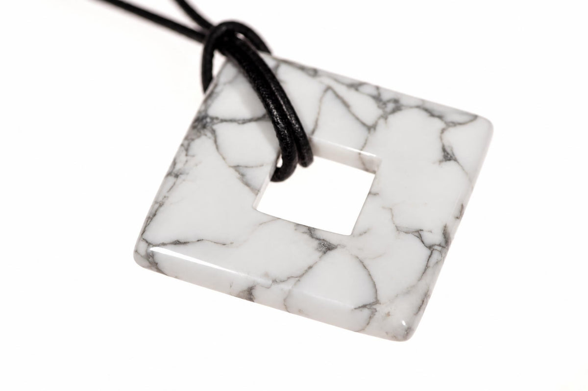 A square white pendant with grey veining and a central hole, threaded on a black cord against a white background.
