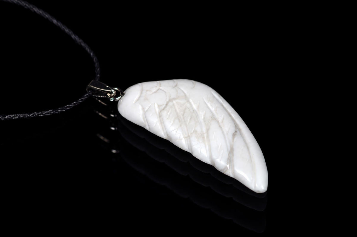 A white pendant shaped like a wing with carved lines, attached to a dark cord on a black reflective surface.