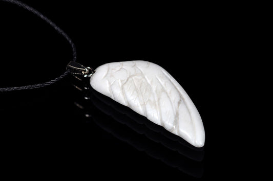 A white pendant shaped like a wing with carved lines, attached to a dark cord on a black reflective surface.