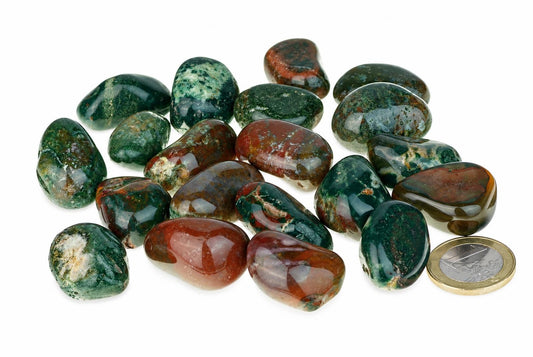 A pile of polished Irai jasper stones in green and reddish-brown patterns on a white surface, with a coin for scale.