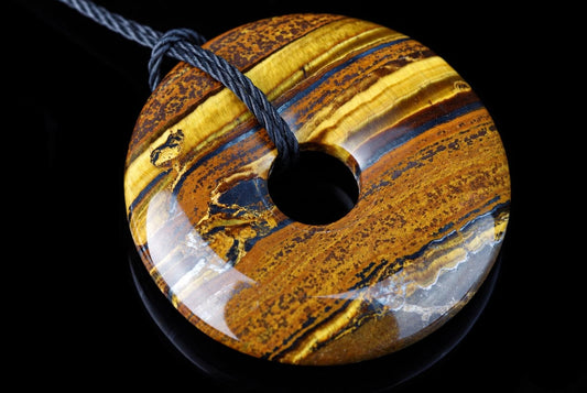 A polished donut-shaped pendant with yellow, brown and blue stripes on a dark surface.