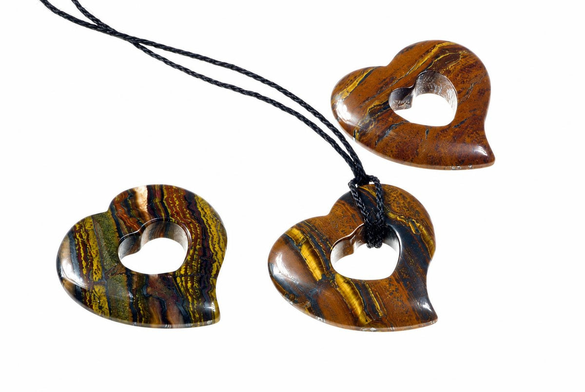 Three polished heart pendants with open centers and brown, gold-colored and dark bands are arranged on white, with a black cord through one pendant.