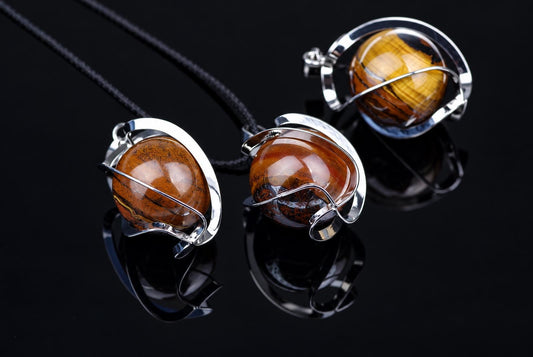 Three silver-toned pendants with polished brown and black striped spheres on a dark reflective surface.