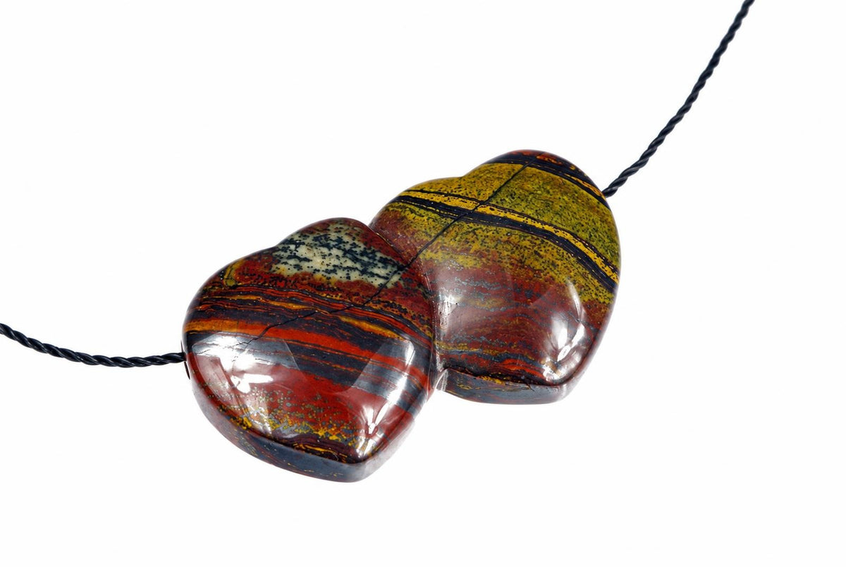A polished pendant with a heart shape, featuring red, yellow and black stripes on a white background.