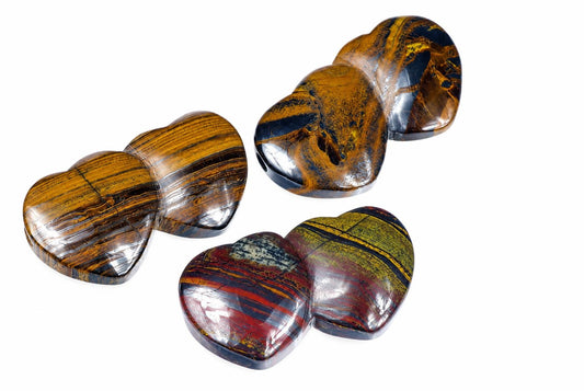 Three polished, heart-shaped stones with striped patterns in brown, black, red and yellow on a white background.