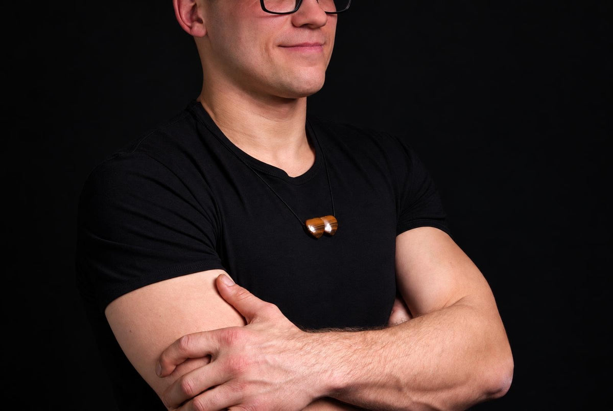 A man wears a necklace with two polished brown stones on a dark surface.