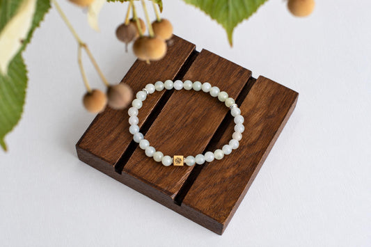 A bracelet with pale green beads and a gold-toned square charm rests on a dark wooden surface.