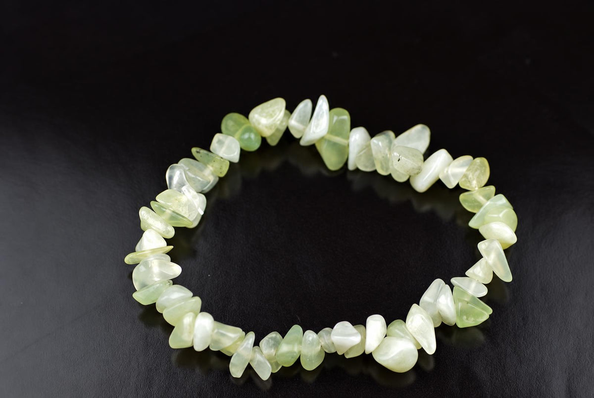 A bracelet made of irregular chips in pale green and white, arranged in a circle on a dark surface.