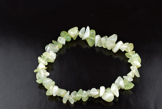 A bracelet made of irregular chips in pale green and white, arranged in a circle on a dark surface.