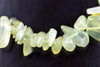 A strand of pale green and white polished chips, possibly jade, arranged on a dark surface.