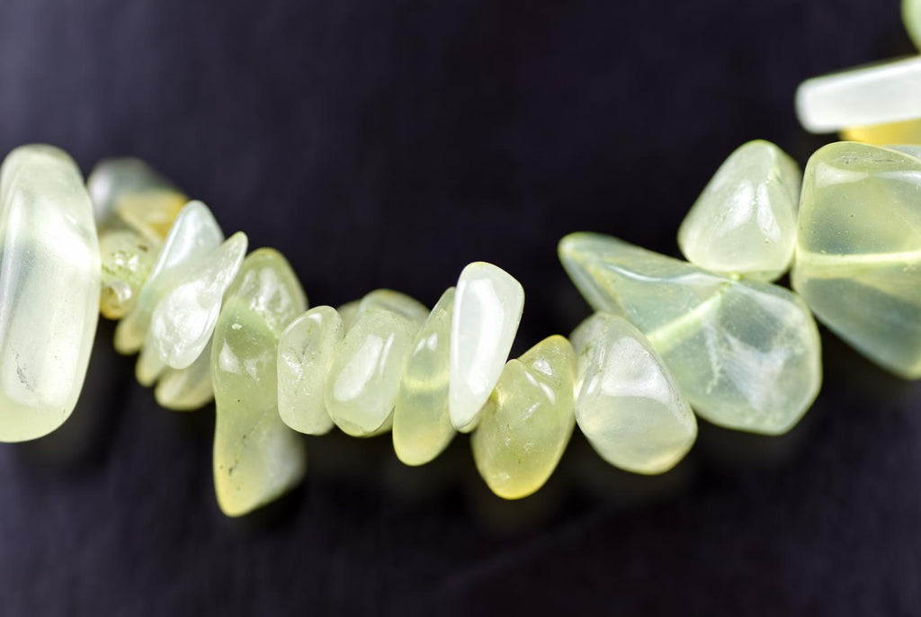 A strand of pale green and white polished chips, possibly jade, arranged on a dark surface.