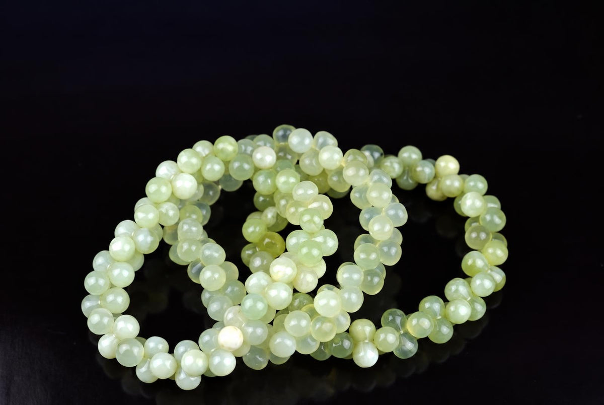 A strand of round, pale green beads with a smooth, glossy finish rests on a dark surface.
