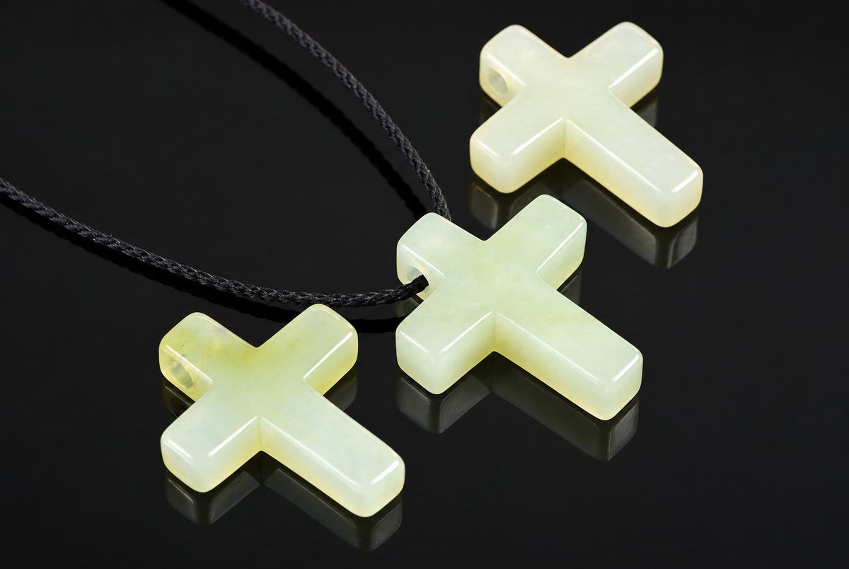 Three pale yellow cross-shaped pendants on dark cords rest on a dark reflective surface.