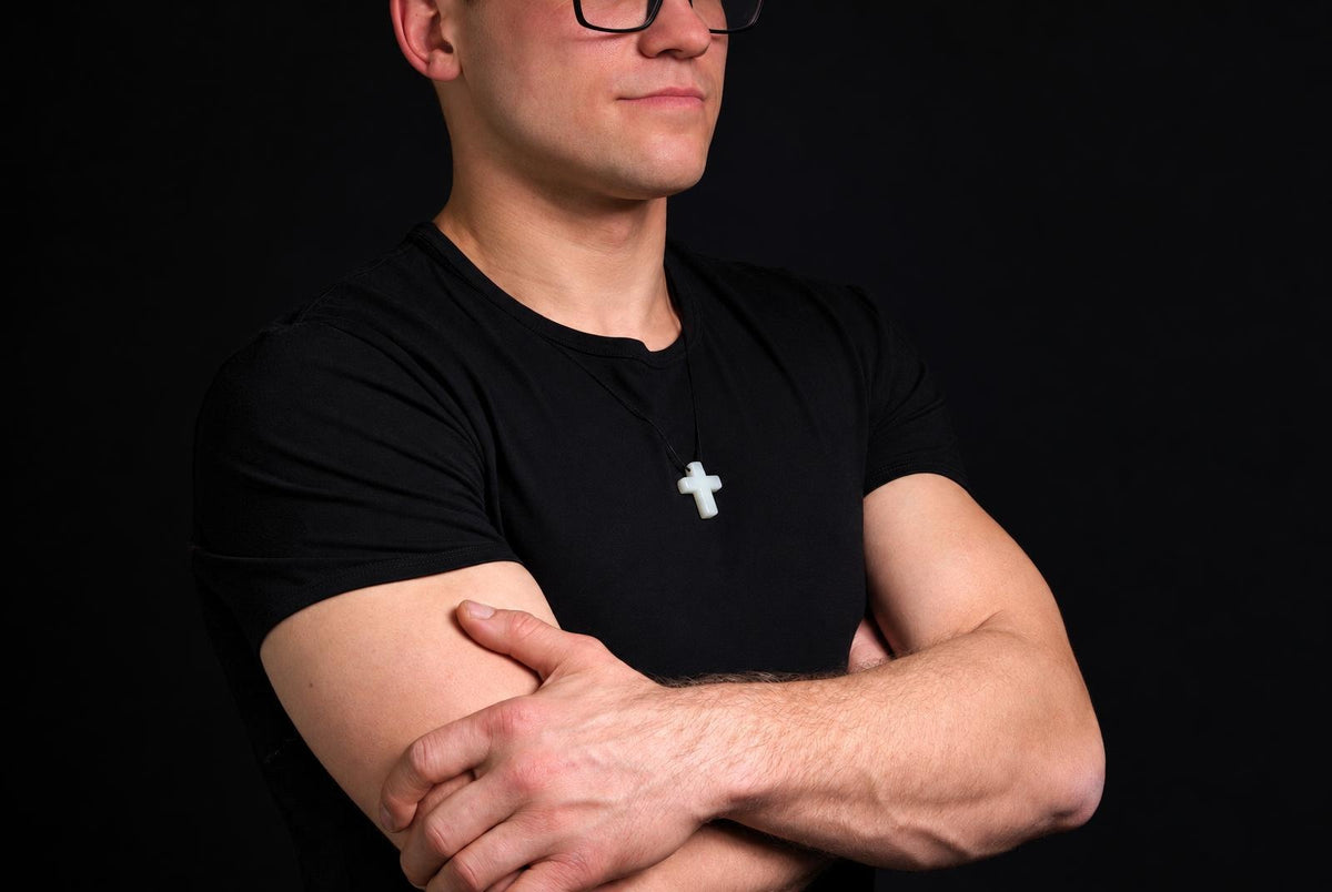 A man in a black t-shirt wears a light green jade cross pendant on a dark surface.