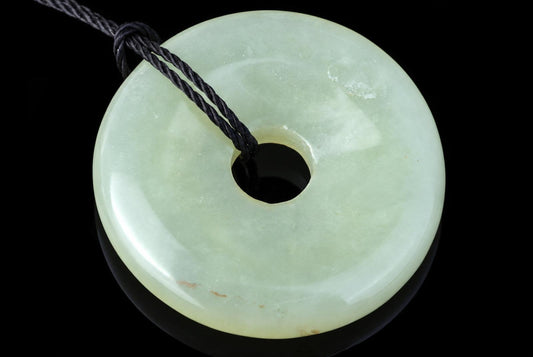 A pale green jade pendant shaped like a donut with a central hole, threaded on a dark cord against a black background.