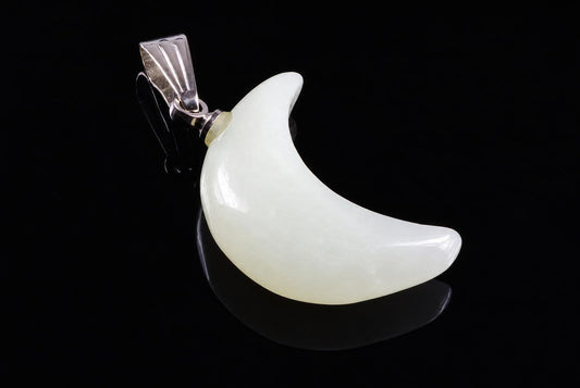 A silver-toned pendant with a pale, crescent-shaped stone on a dark surface.