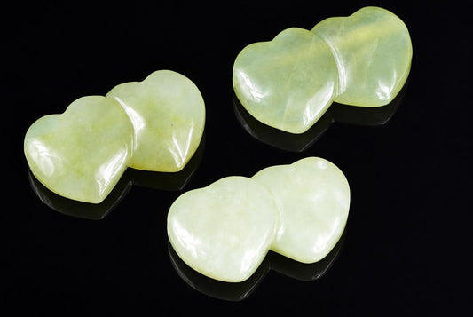 Three pale green jade pendants shaped like two joined hearts, displayed on a dark reflective surface.