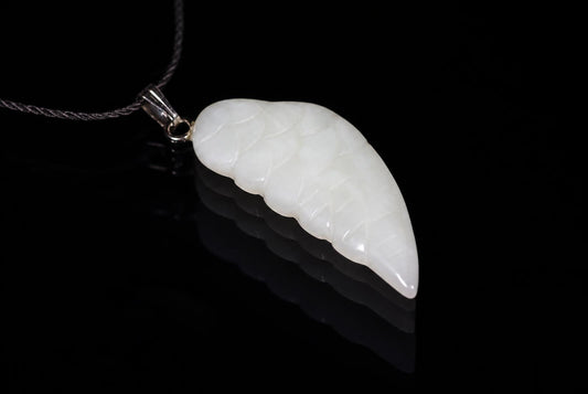 A white jade pendant shaped like a wing with carved lines, hanging from a silver-toned bail on a dark cord against a black reflective surface.