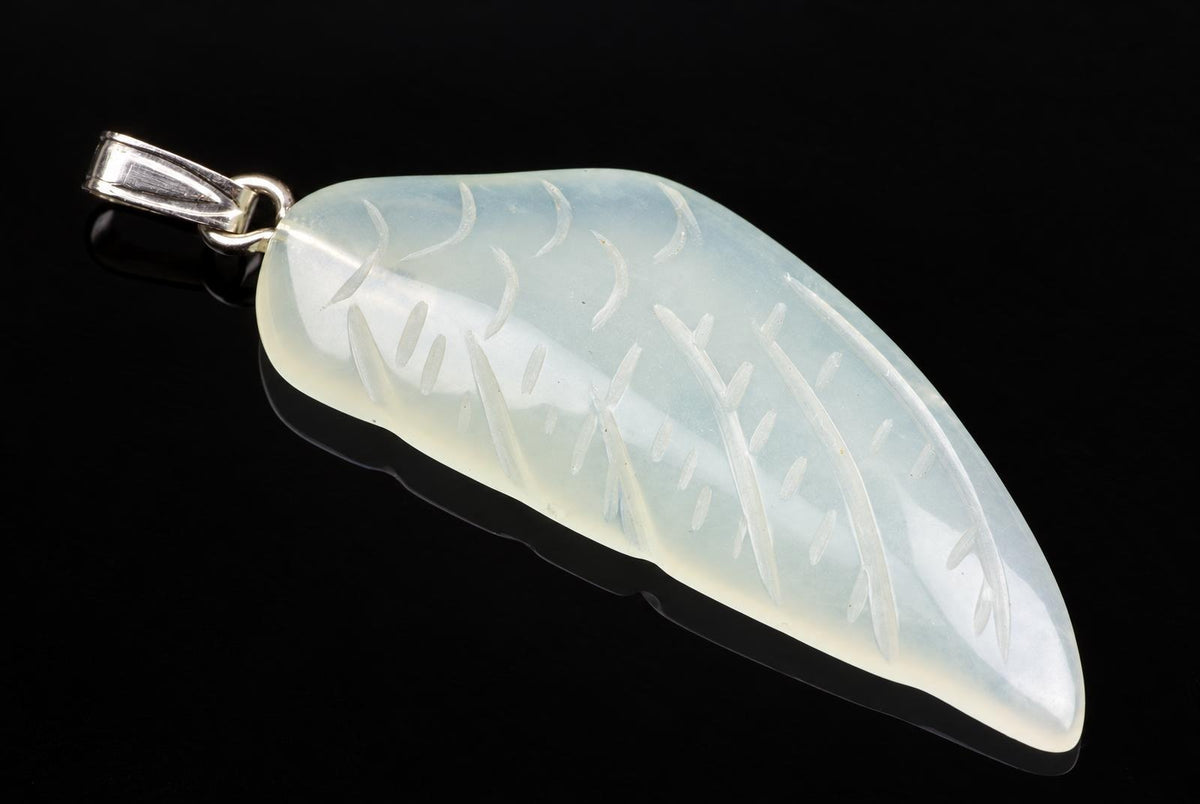 A silver-toned pendant with a pale, translucent stone carved into a wing shape, set against a dark surface.