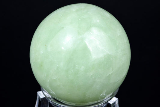 A polished, pale green spherical stone rests on a clear stand against a dark background.