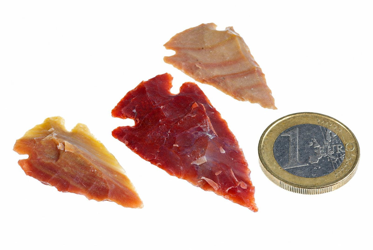 Three arrow-shaped jasper pendants in red, yellow and pale brown lie on a white surface next to a one euro coin.