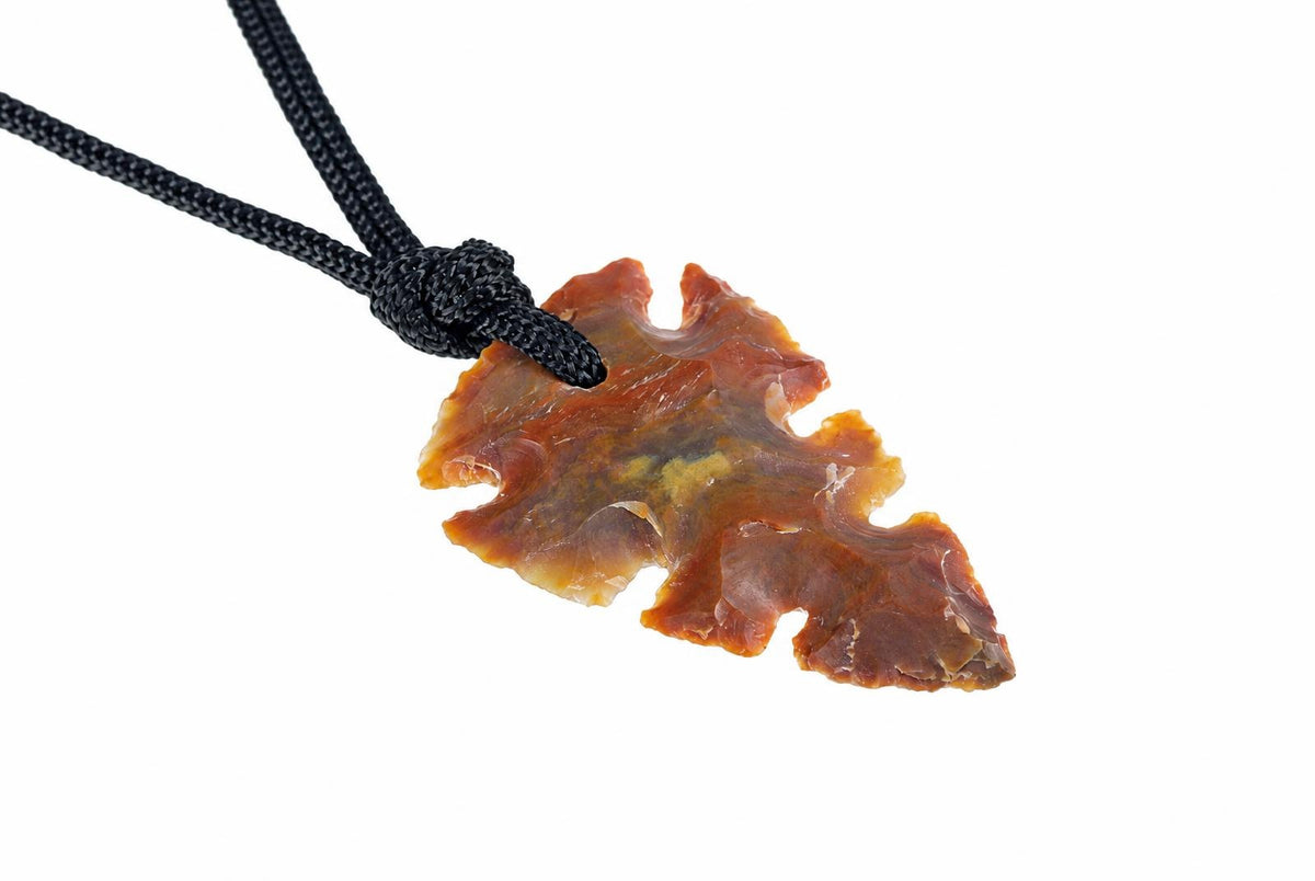 A jasper pendant shaped like an arrowhead, with brown and yellow tones, hangs from a black cord against a white background.